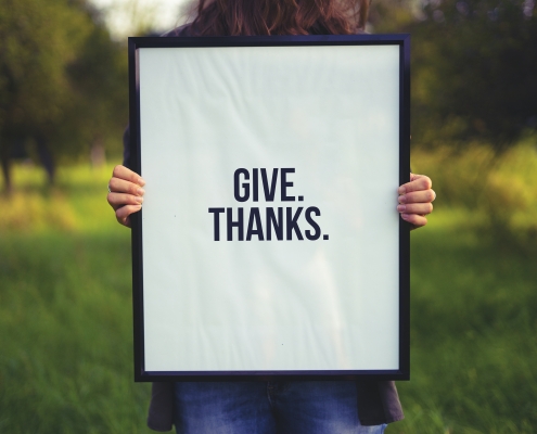 simon-maage-KTzZVDjUsXw-unsplash give thanks on white sign held in front of a person; sharing gratitude