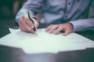 scott-graham-OQMZwNd3ThU-unsplash image of hands holding a pen, appears to be writing on a document on a table