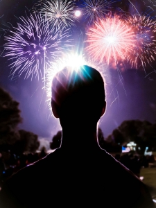 spenser-sembrat-qBfKWYDewMw-unsplash silhouette of an adult head in foreground, colorful fireworks in background against night sky; 4th of July
