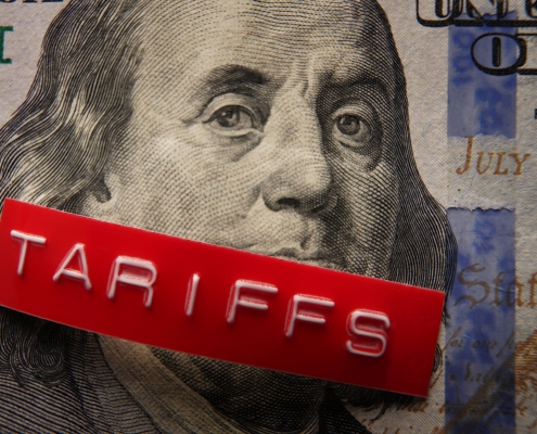 Red Tariffs label on a hundred dollar bill face of Benjamin Franklin from the 100 dollar bill with the word "tariffs" in white letters on a red background across Ben's mouth; current events - tariffs - April 2025; Current Events - July 2025; shifting global oil flow