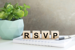 rsvp acronym request for a response from the invited person on wooden cubes on the office table. blocks spelling RSVP on top of a notebook in front of a gray background, with a plant to the left; Westlark Advisors Client Appreciation Event
