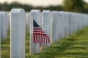 close up of small American flag in row of headstones in military cemetery; Memorial Day - Remembering