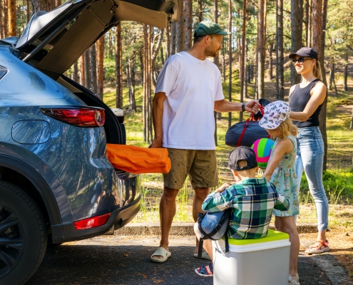 family with kids remove the camping supplies from car trunk at forest. summer holidays, road trip A family, dad, mom, son and daughter, packing a car, Labor Day - the importance of hard work