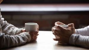 Close up woman and man holding cups of coffee on table two coffee cups facing each other with hands around each cup; 7 principles fierce conversations