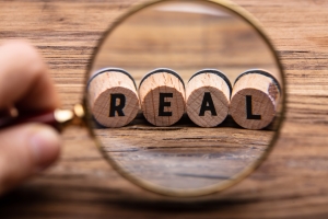 Hand Holding Magnifying Glass In Front Of Real Text magnifying glass in front of corks with letters spelling the word "real"; 7 principles fierce conversations