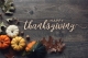 the words Happy Thanksgiving on a gray, wood like background with pumpkinds, gourds and leaves at the bottom left; Giving Thanks
