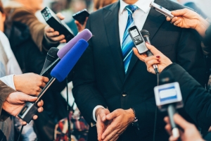 Media interview man in suit surrounded by microphones; words matter
