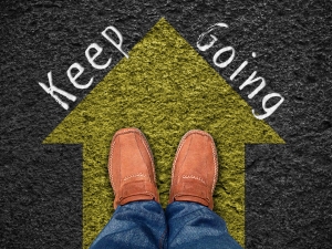 Inspiration quote : " Keep going" men's shoes on yellow arrow against black background with words "keep going"; hope at Easter