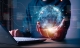 international market highlight; hand holding transparent globe in front of an open laptop