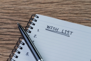 Wish list concept, pen on white paper note pad with handwritten headline as Wish List and numbers listed on wood table in soft tone, things wanted or next time purchase notebook with words "wish list" at top and pen across it against wood background; 250 Anniversary of Independence