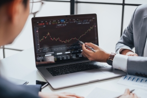 Businessman talking about investment stock market and graph from computer laptop with broker trader, giving money plan management and analysis 2 people looking at financial market information on a laptop screen; locational and time spreads