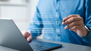 Checklist business report concept. Check mark opinion. Tick checkbox survey. Checkmark. man in blue shirt sitting at a desk in front of laptop with pen in hand and transparent checklist in air, acting like he's checking a box